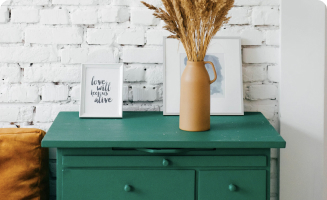 Green dresser with framed artwork and a vase of dried flowers